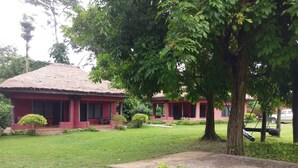 A red building with a thatched roof, surrounded by well-maintained grass and trees. - Big Foot Safari Lodge (Wli)