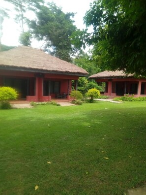 A building with a thatched roof and red walls, surrounded by well-maintained grass and small bushes. - Big Foot Safari Lodge (Wli)
