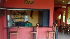 A bar area with a red wall, wooden chairs, and ceiling fans. - Big Foot Safari Lodge (Wli)