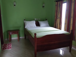 A bedroom with a wooden bed, green walls, a small bedside table, and a window with curtains. - Big Foot Safari Lodge (Wli)