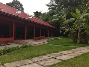 A red building with a satellite dish, surrounded by lush greenery and banana plants. - Big Foot Safari Lodge (Wli)
