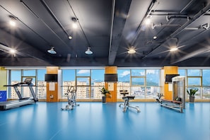 A gym with exercise equipment, large windows, and a city view. - Zhangjiajie Huatian Hotel (Zhangjiajie)