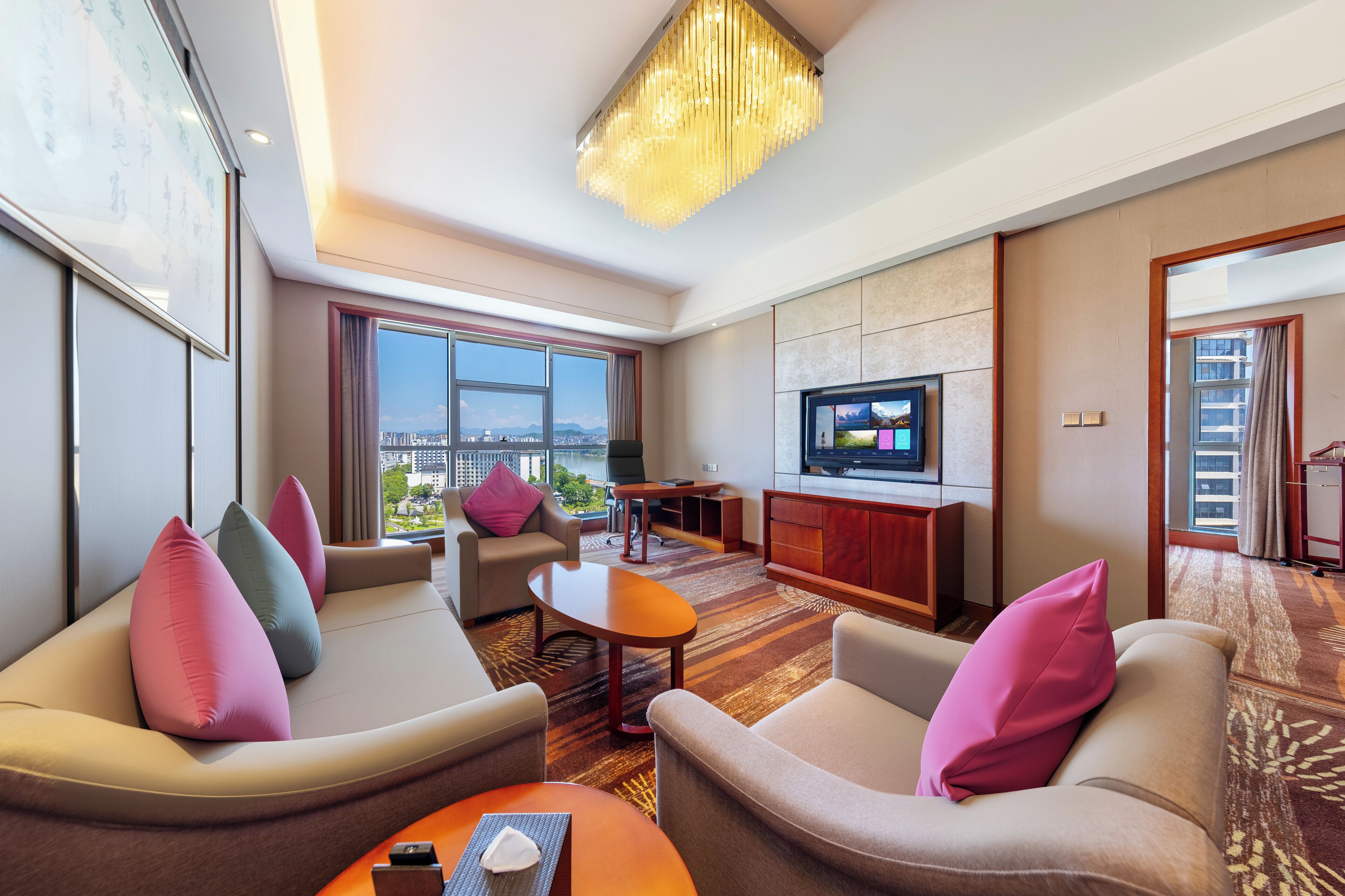 Une chambre d’hôtel moderne, dotée d’un canapé, d’une table basse, d’un téléviseur et offrant une vue sur le paysage urbain.