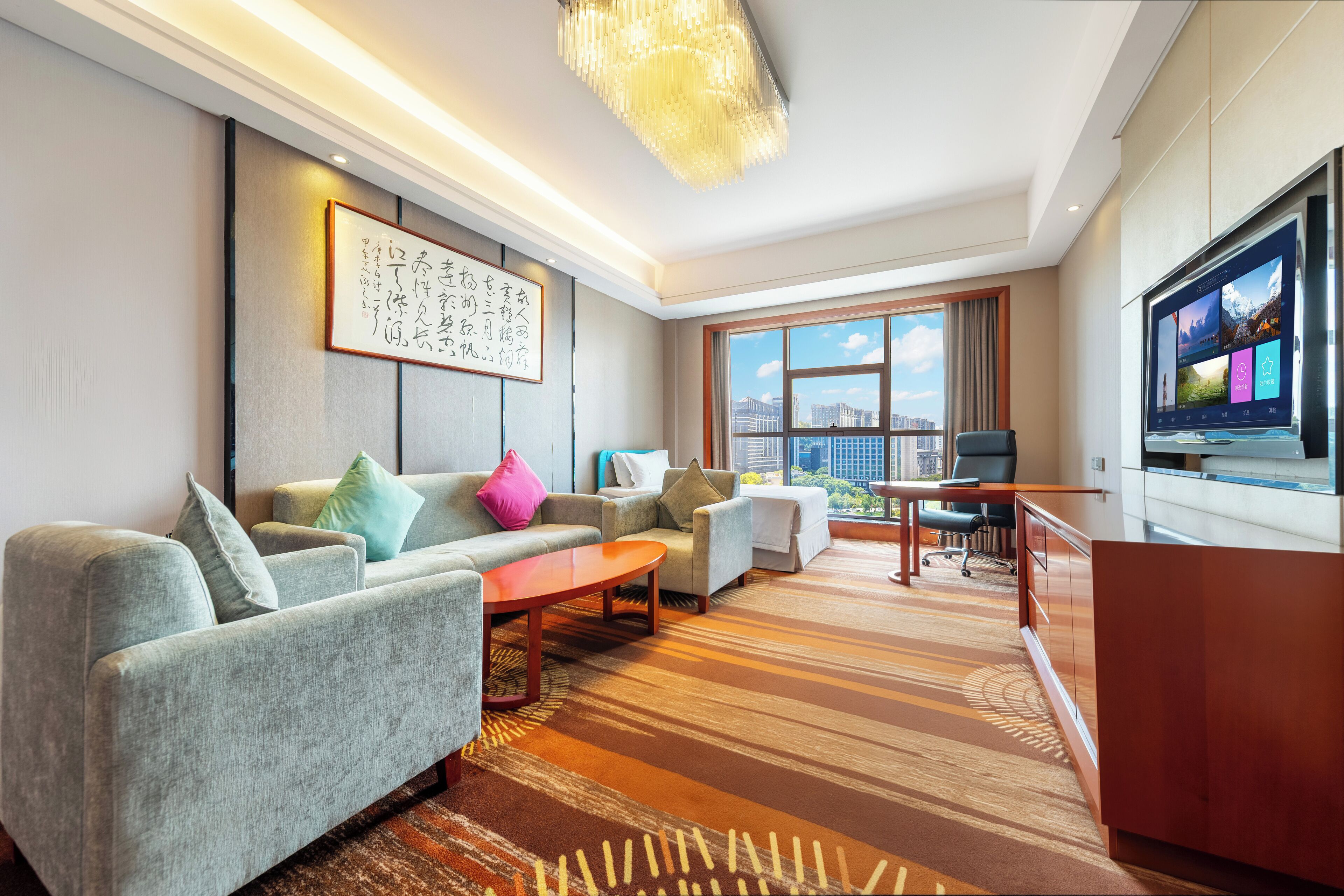 A modern hotel room with a large flat-screen TV, a sofa set, a coffee table, and a view of the cityscape.