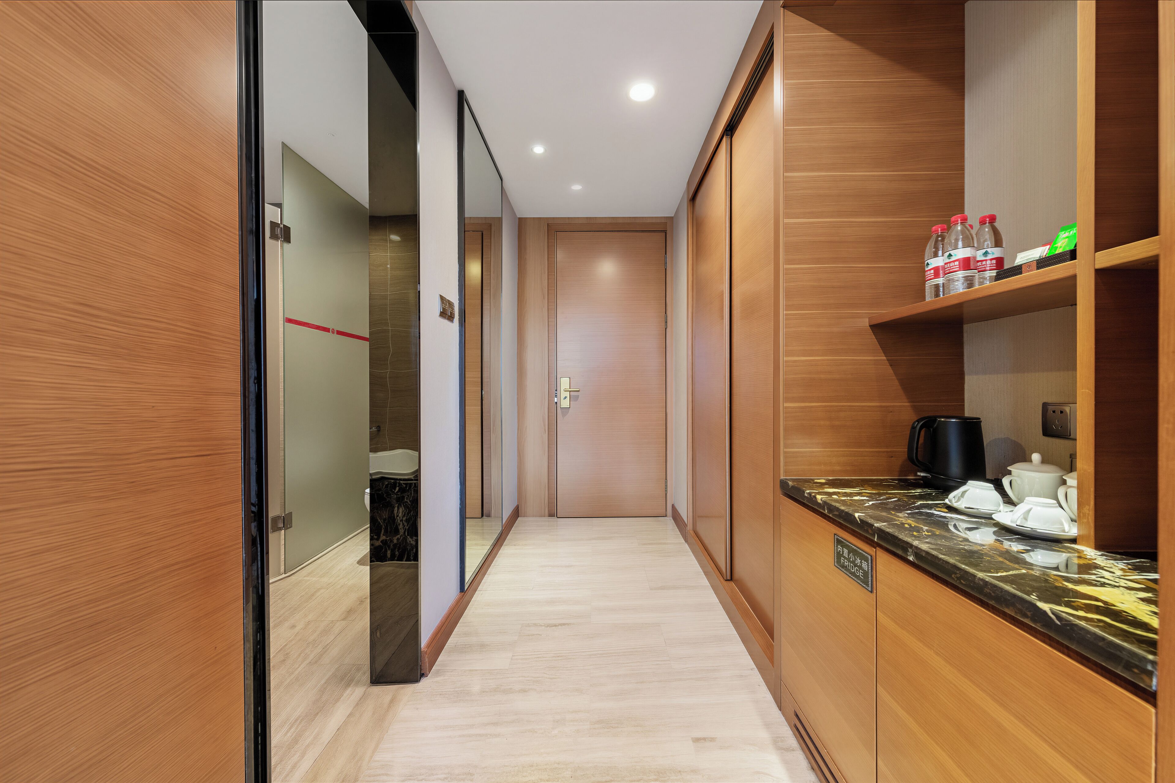 A hotel corridor with wooden walls, a marble-topped counter with tea service, and a visible door leading to a bathroom.