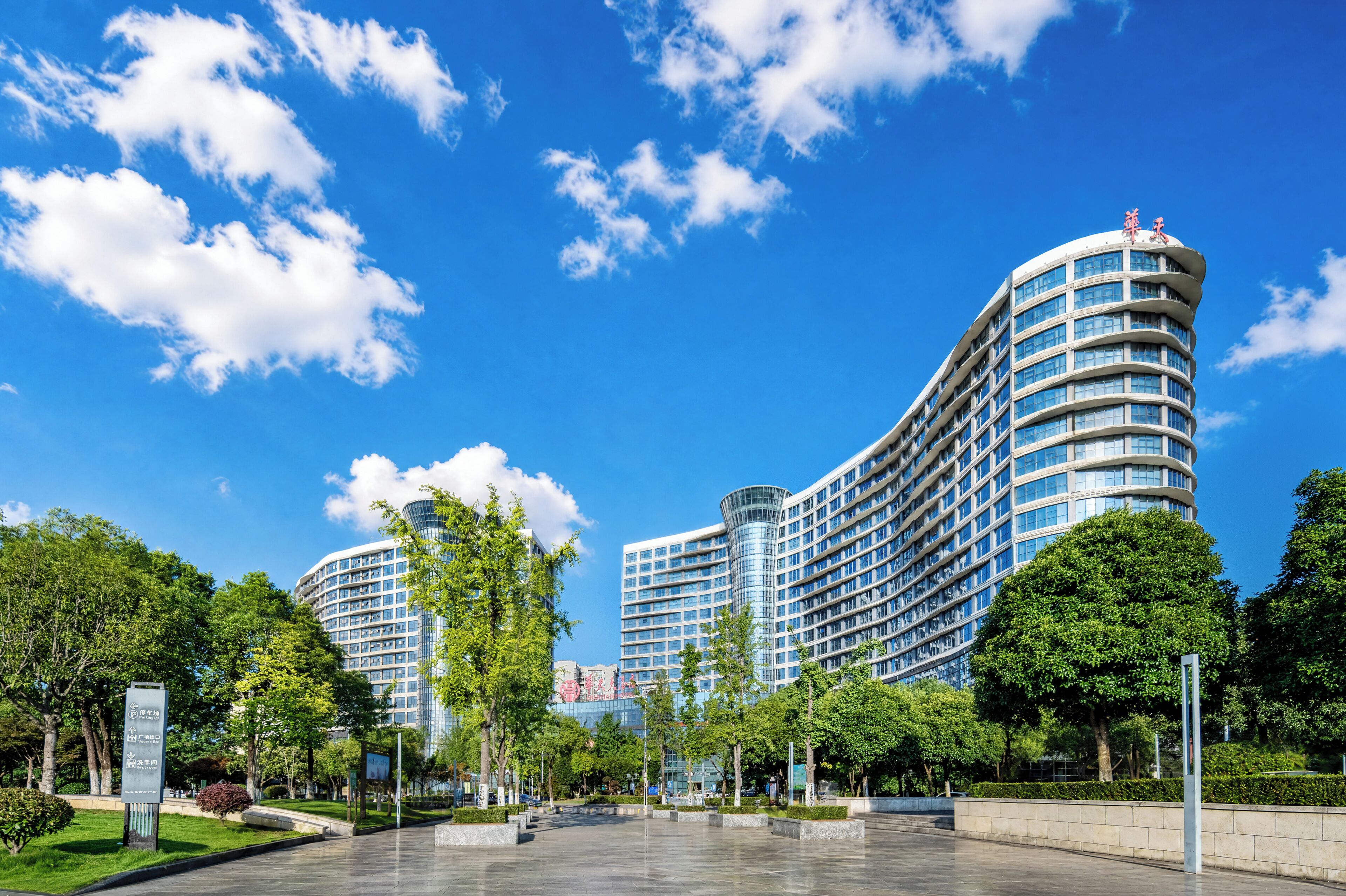 Un hotel moderno con fachada curva, varios pisos y cielo despejado con nubes.
