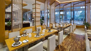 A modern dining area with wooden tables and chairs, large windows, and a view of the city. - Zhangjiajie Huatian Hotel (Zhangjiajie)