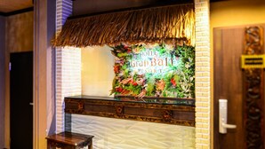Uma área de recepção com decoração temática tropical, um balcão e um pequeno banquinho de madeira.