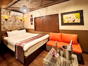 Quarto de hotel com cama, sofá laranja, uma mesinha com garrafa e copos, e um quadro na parede.