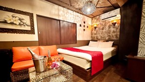 Quarto de hotel com cama, sofá laranja e uma mesa com champanhe e taças.