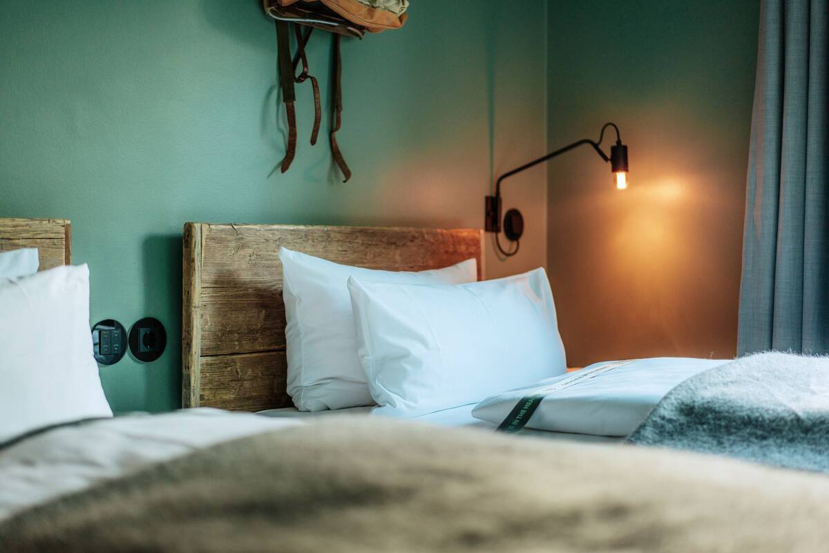 A neatly made bed with white bedding, a wooden headboard, and a wall-mounted lamp.