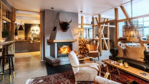 A modern living room with a fireplace, wooden beams, and a large window. - The Hearts Hotel Boutique und Event Resort (Braunlage)