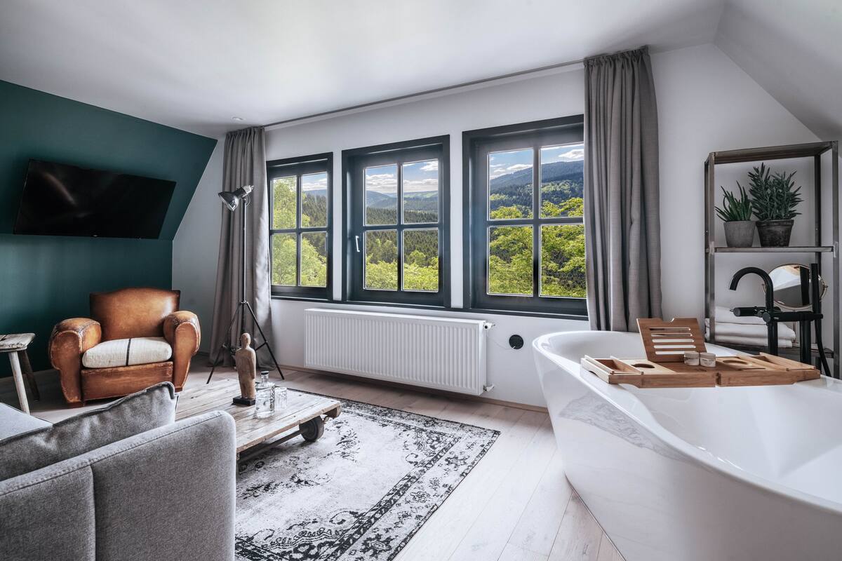 A modern bathroom with a large bathtub, a wooden tray, and a view of a mountainous landscape through large windows.