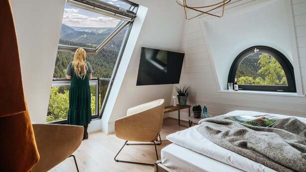 A bedroom with a large window offering a view of a forested mountain range. - The Hearts Hotel Boutique und Event Resort (Braunlage)