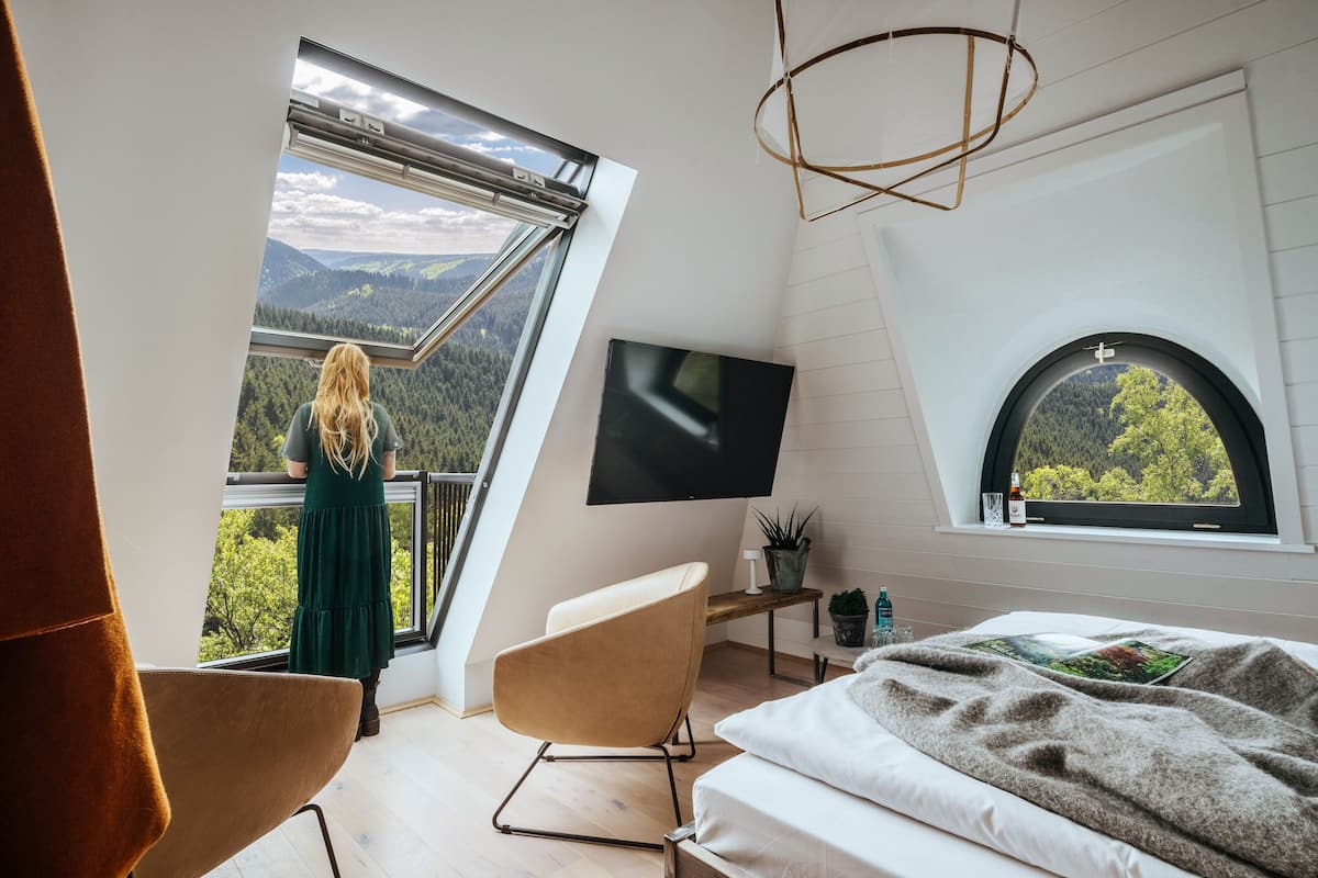 A bedroom with a large window offering a view of a forested mountain range.