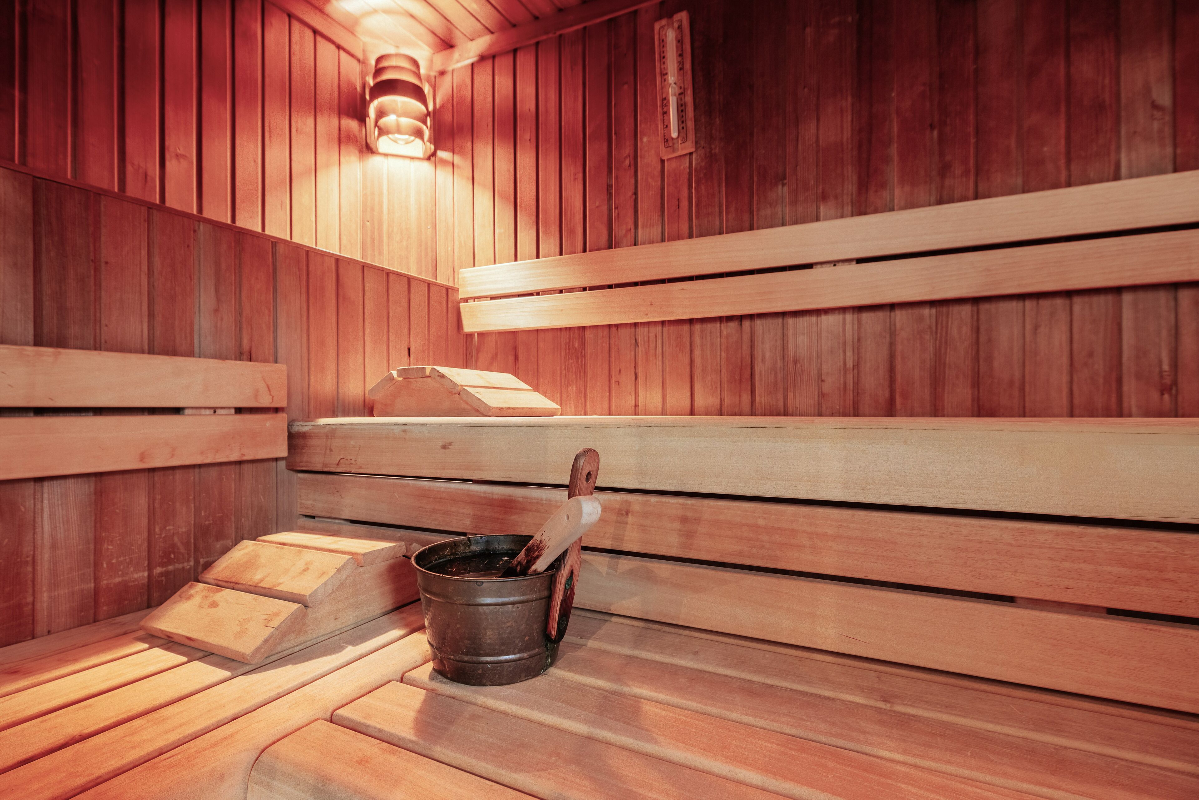 Een houten sauna met banken en een emmer met houten handvat.