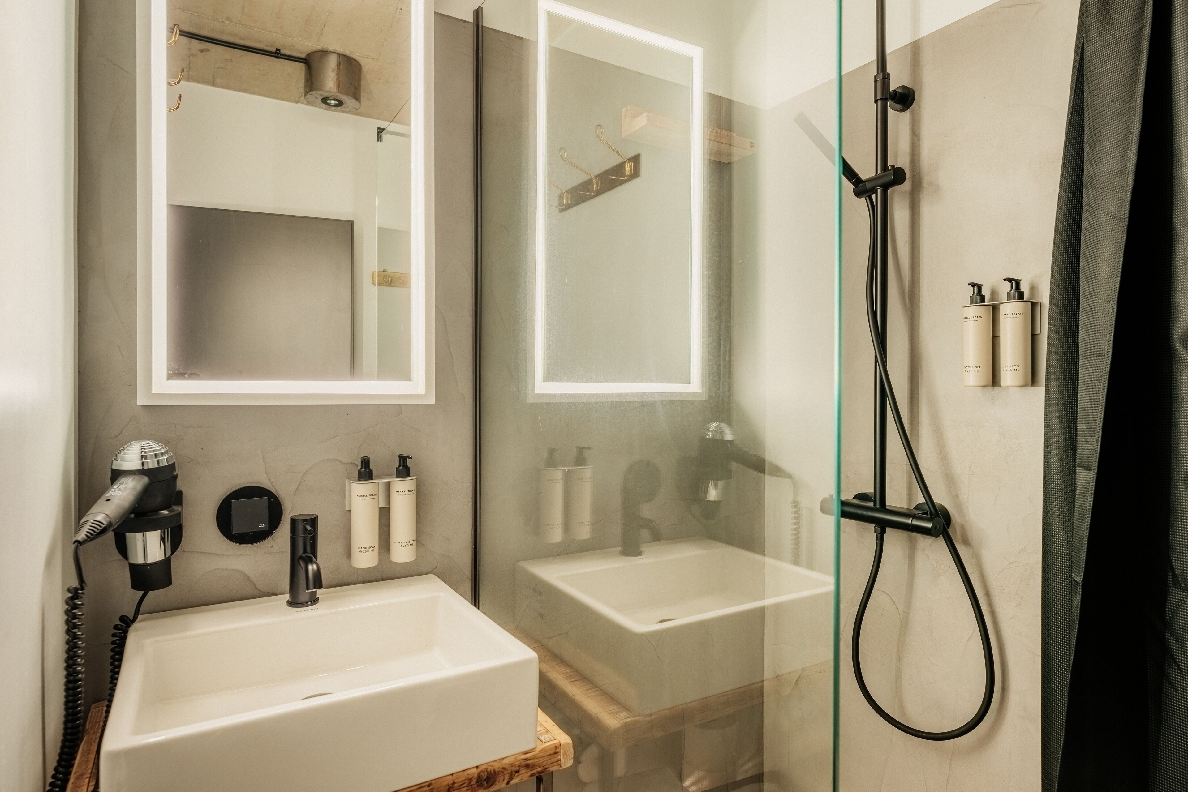 Un baño moderno con un espejo grande, dos lavamanos, un secador de pelo y una ducha.