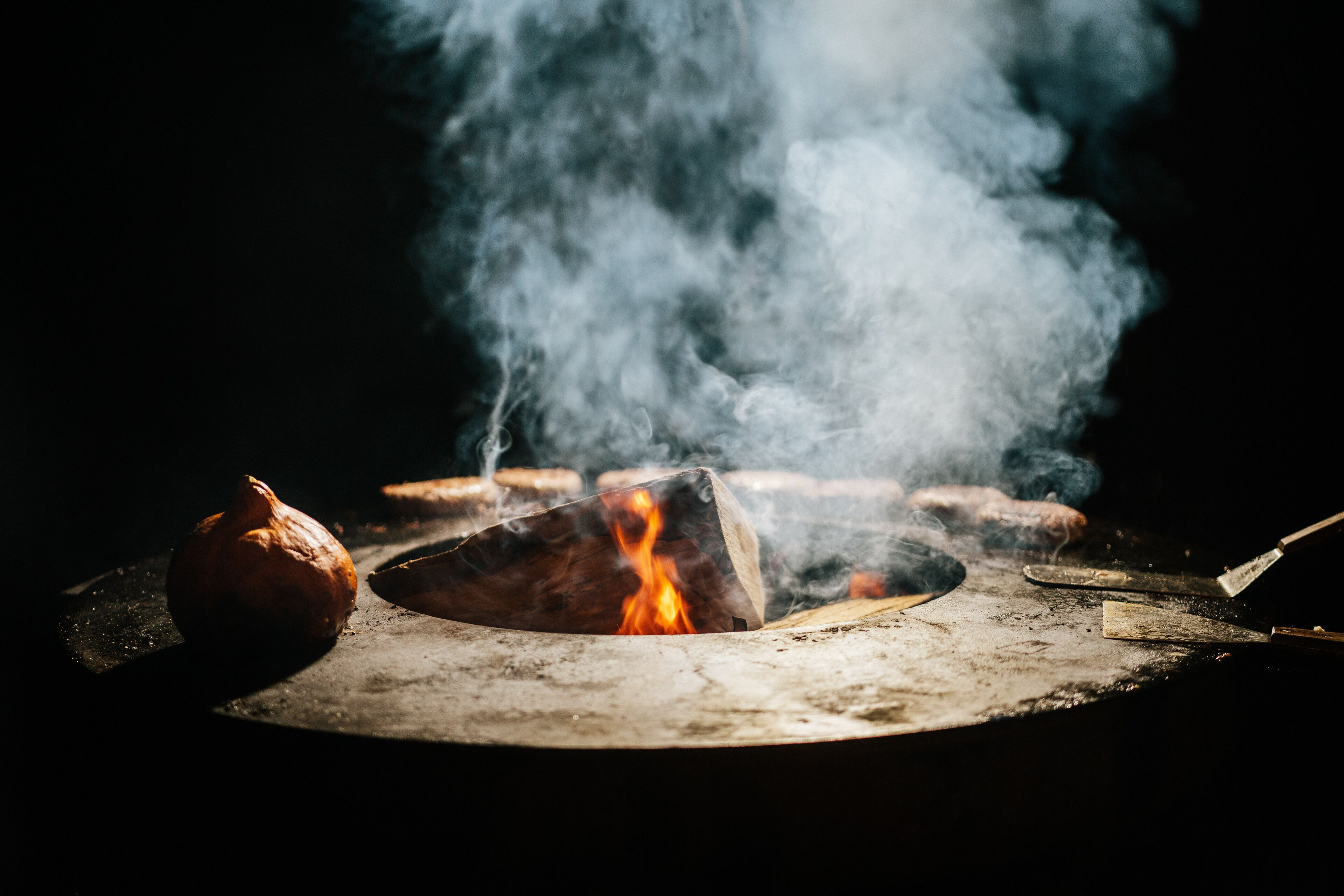 Una fogata con leña y una olla, rodeada de humo.