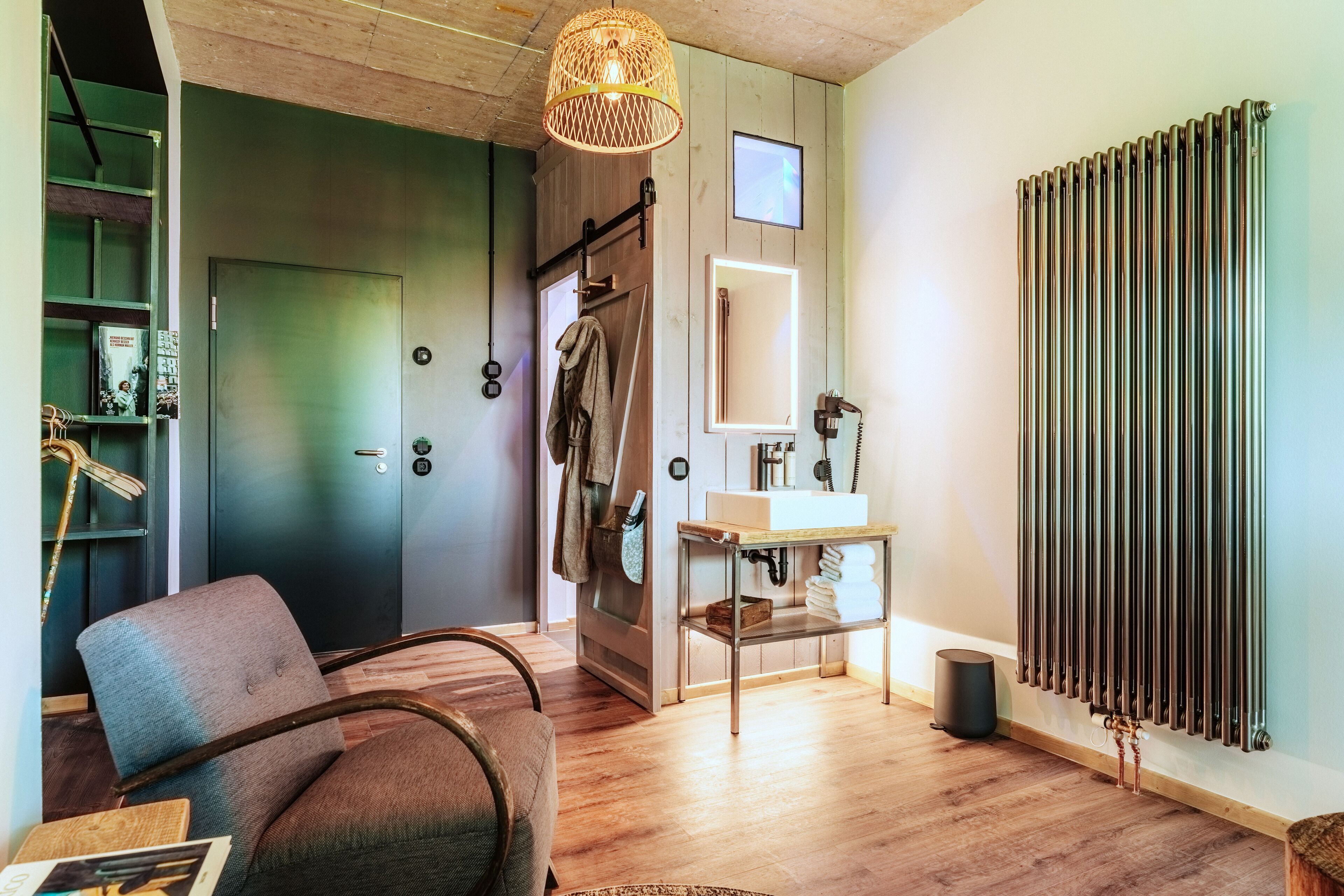 A modern living room with a wooden floor, a grey sofa, a hanging light fixture, and a radiator.