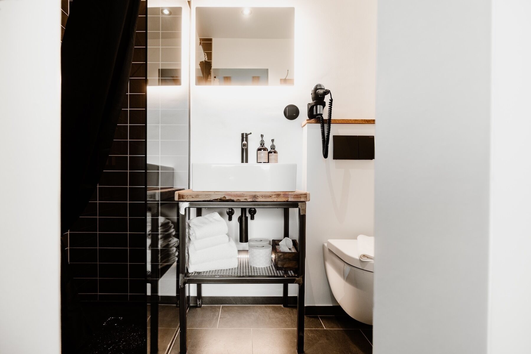 A modern bathroom with a white sink, toilet, and a small table with toiletries.
