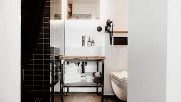A modern bathroom with a white sink, toilet, and a small table with toiletries.