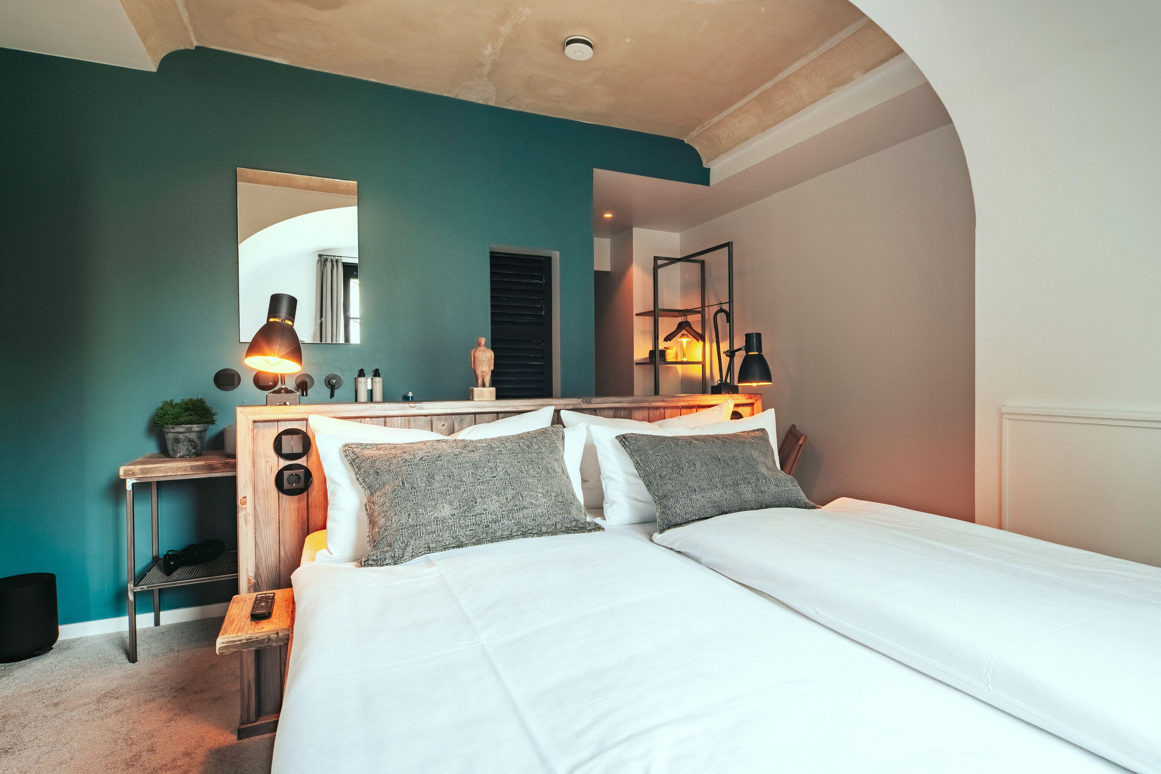 A bedroom with a large bed, a bedside table with a lamp, a mirror, and a wardrobe.