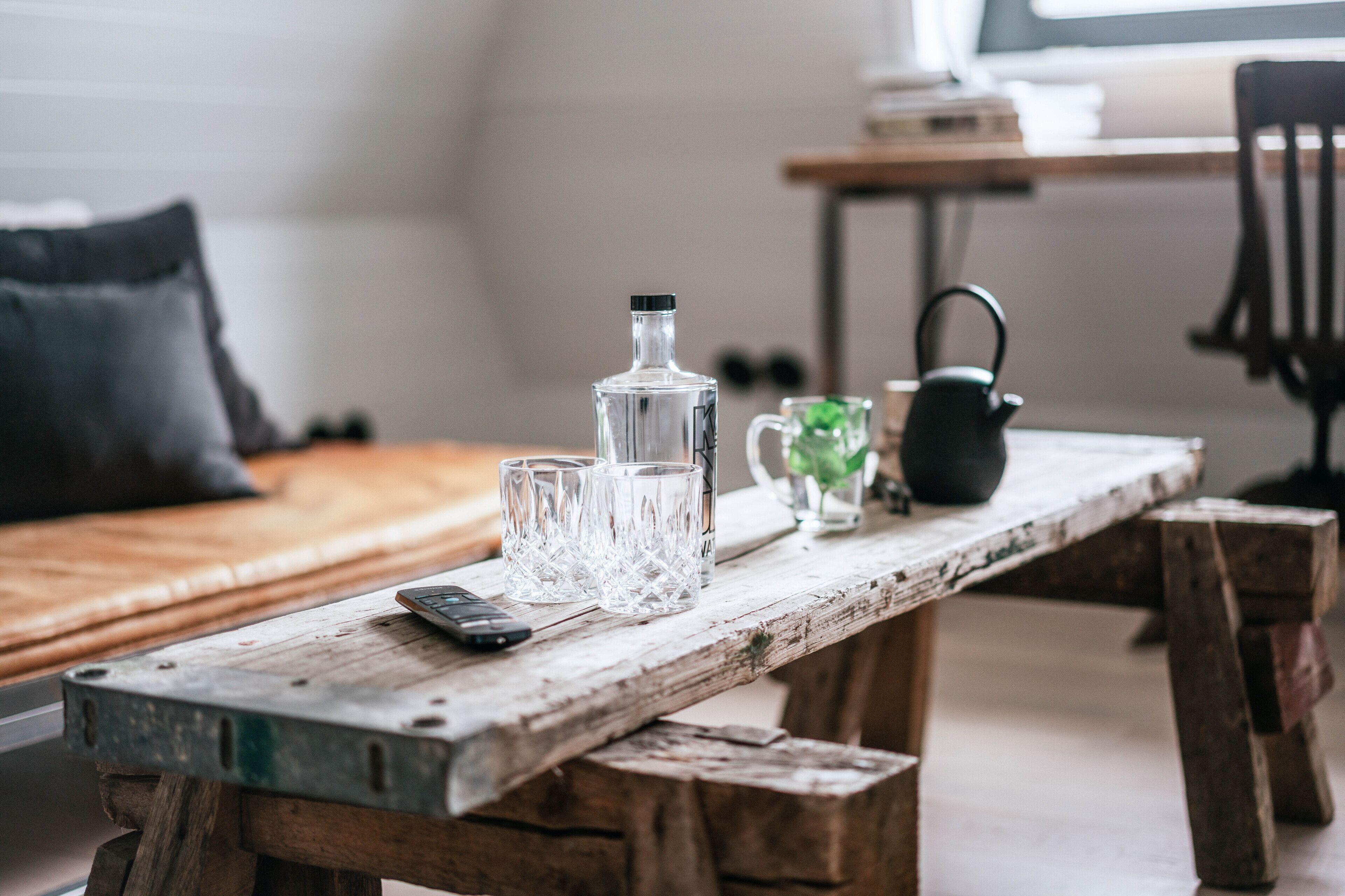A rustic wooden table with a bottle, glasses, a kettle, and a remote control.