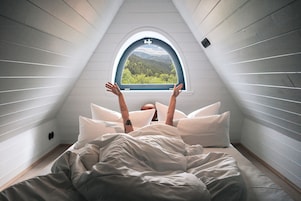 Un dormitorio con techo inclinado y ventana con vistas a un bosque.