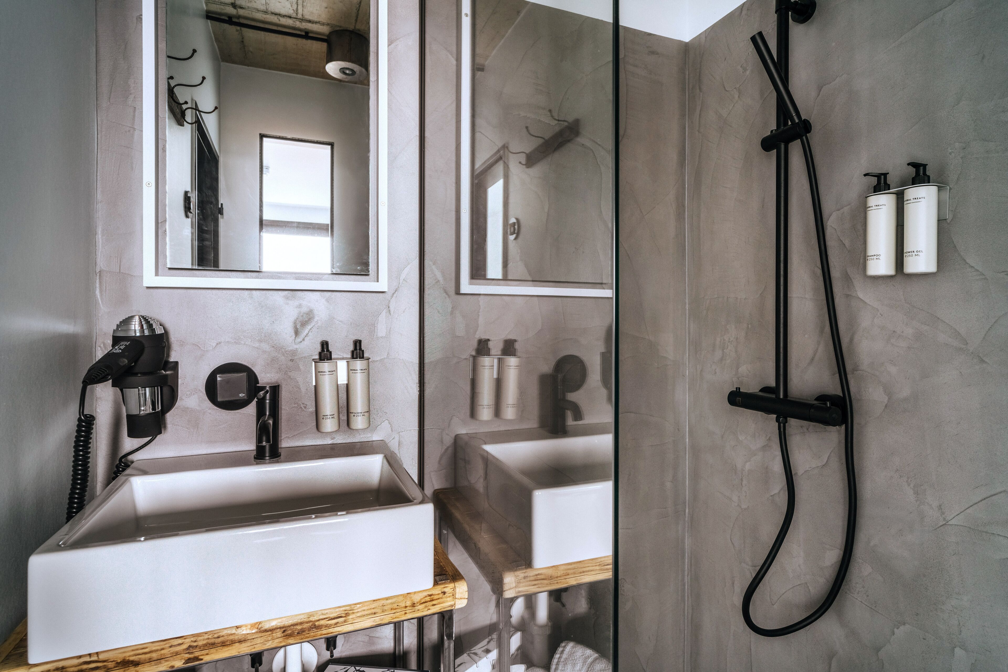 Ein Badezimmer mit großem Spiegel, zwei Waschbecken, einer Dusche und einem Haartrockner auf einem Ständer.
