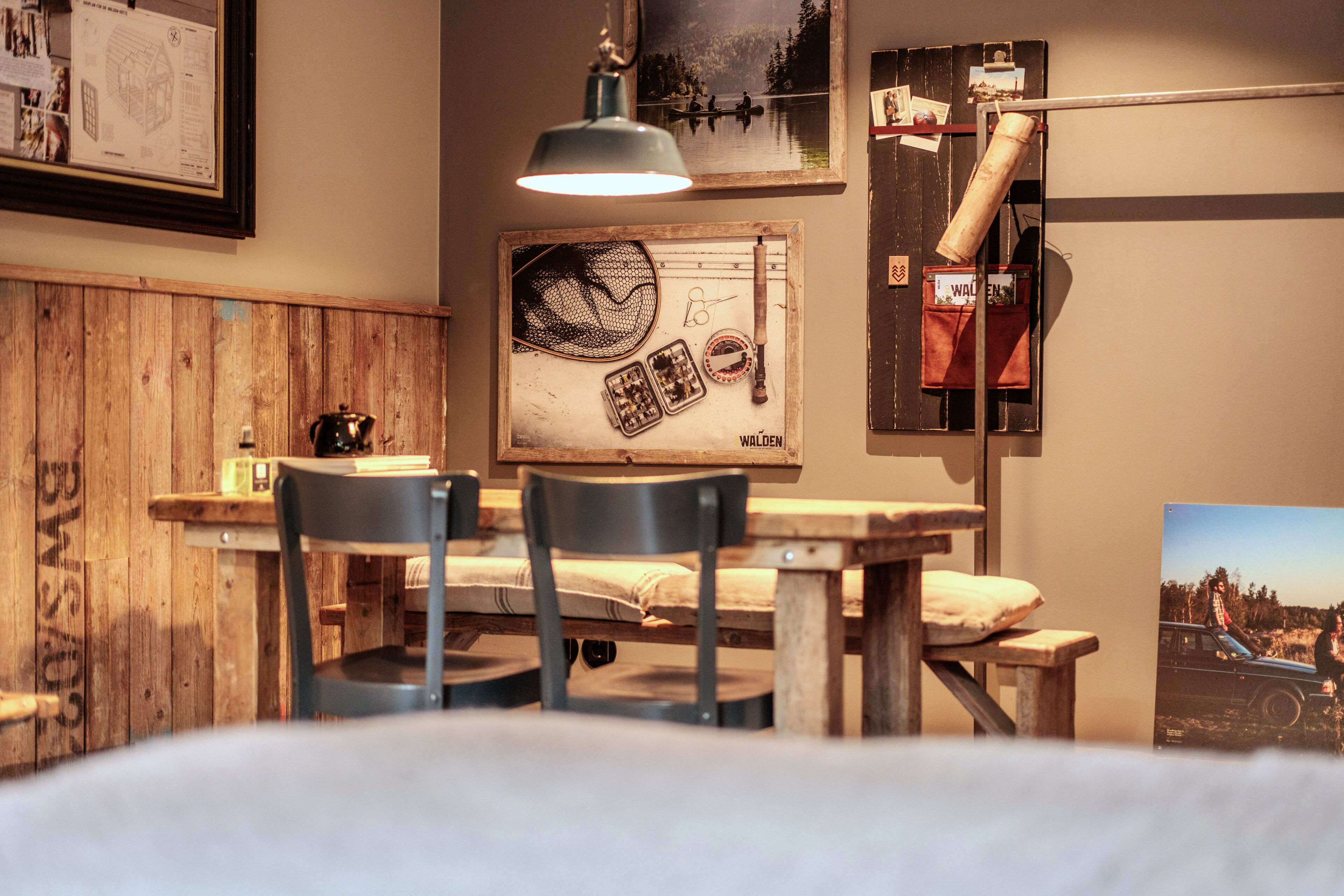 A rustic room with a wooden table, two chairs, a hanging lamp, and a framed picture on the wall.