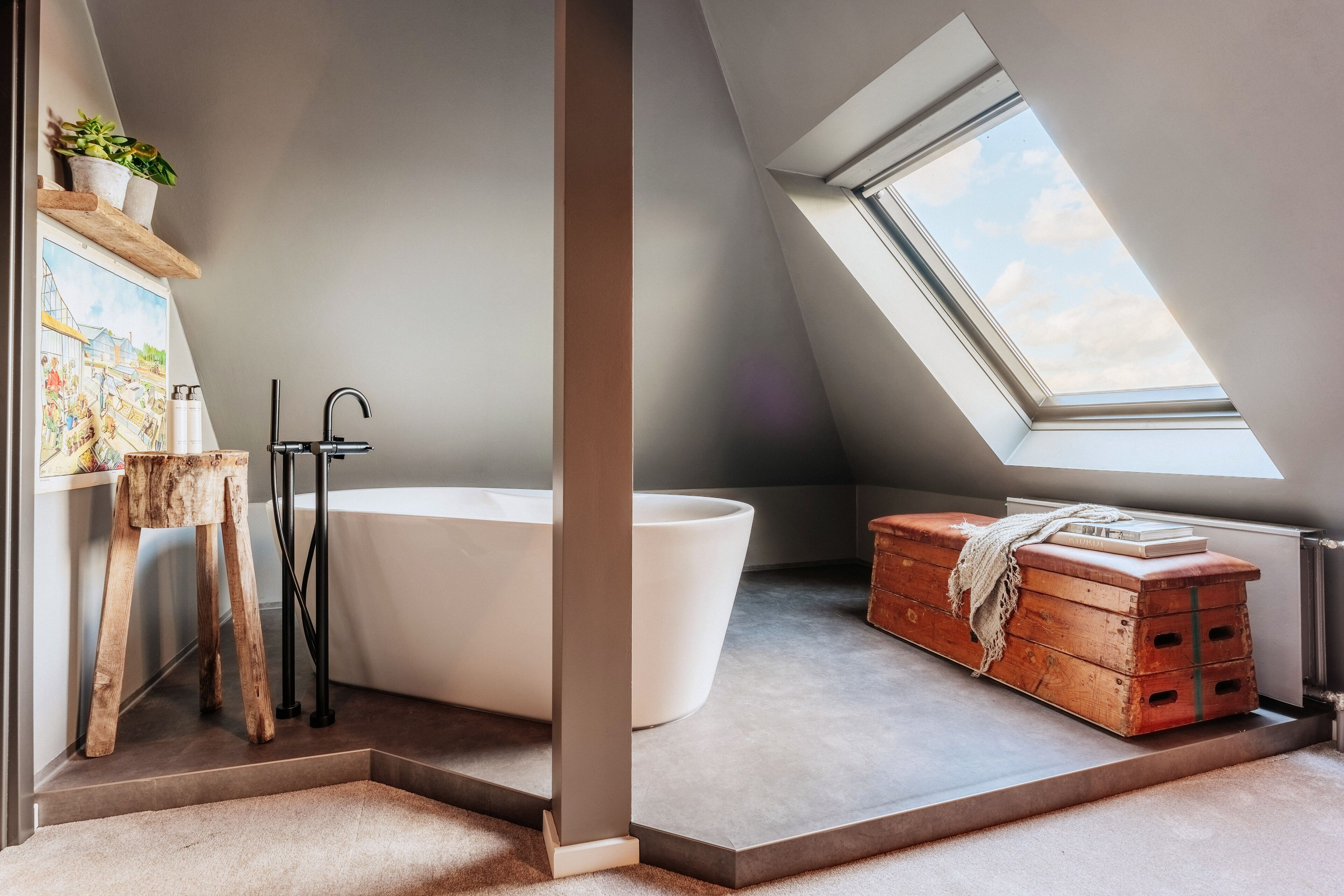 A modern bathroom with a freestanding bathtub, a wooden stool, a painting, and a skylight.