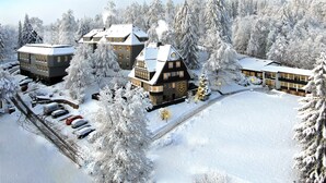 A snow-covered resort with multiple buildings, including a large hotel and smaller cabins, surrounded by dense, snow-laden trees. - The Hearts Hotel Boutique und Event Resort (Braunlage)