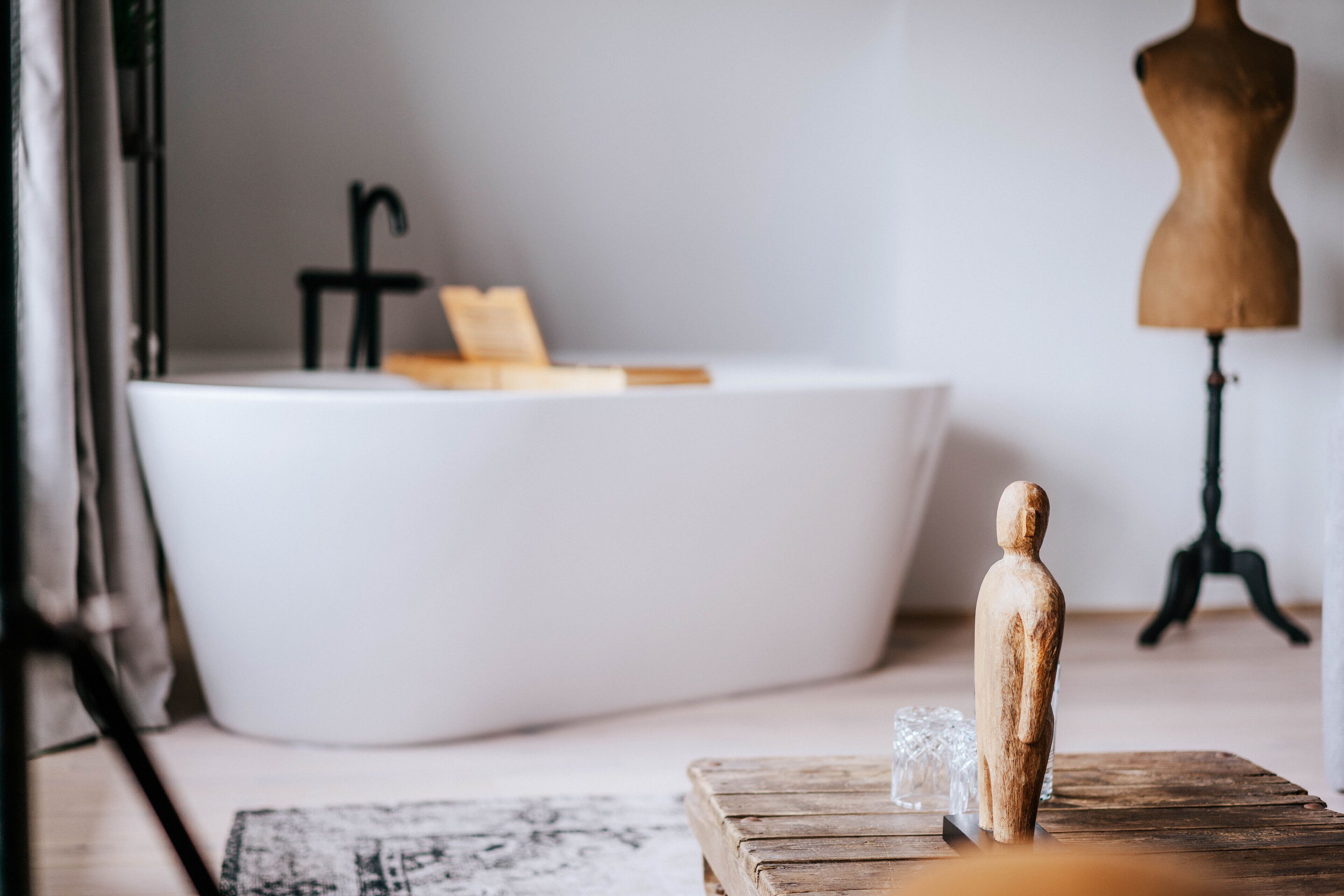 A modern bathroom with a freestanding bathtub, a wooden mannequin, and a small table with a glass.