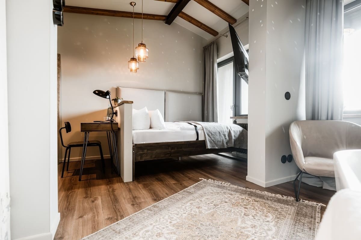 A bedroom with a bed, a desk, a chair, and a large window.