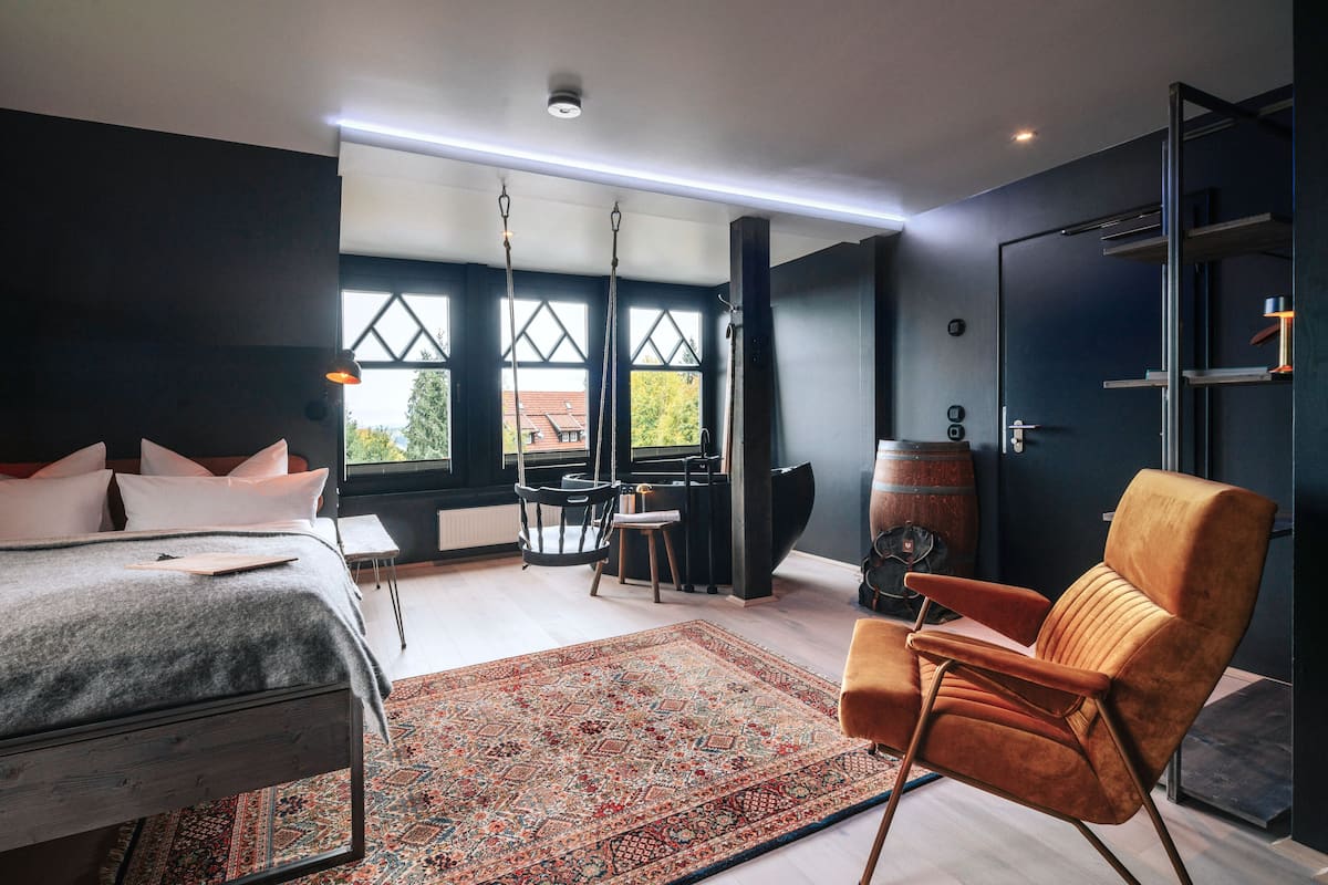 A modern bedroom with a bed, a seating area with a chair, a table, and a large window with a view.