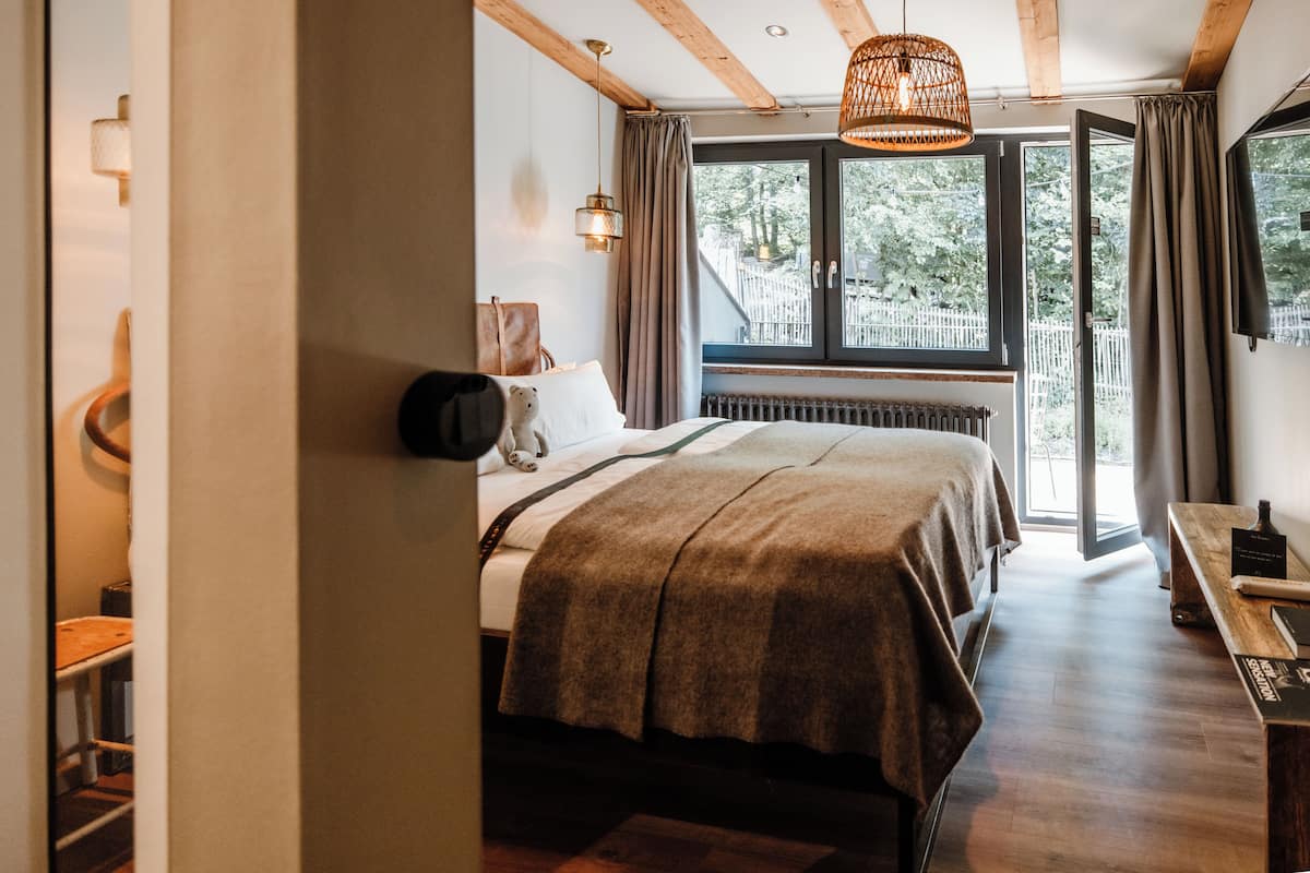A bedroom with a bed, a wooden bench, a hanging light fixture, and a view of the outdoors.