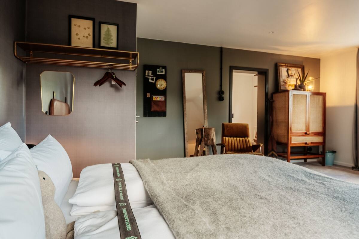 A bedroom with a bed, a wardrobe, a mirror, and a wall clock.