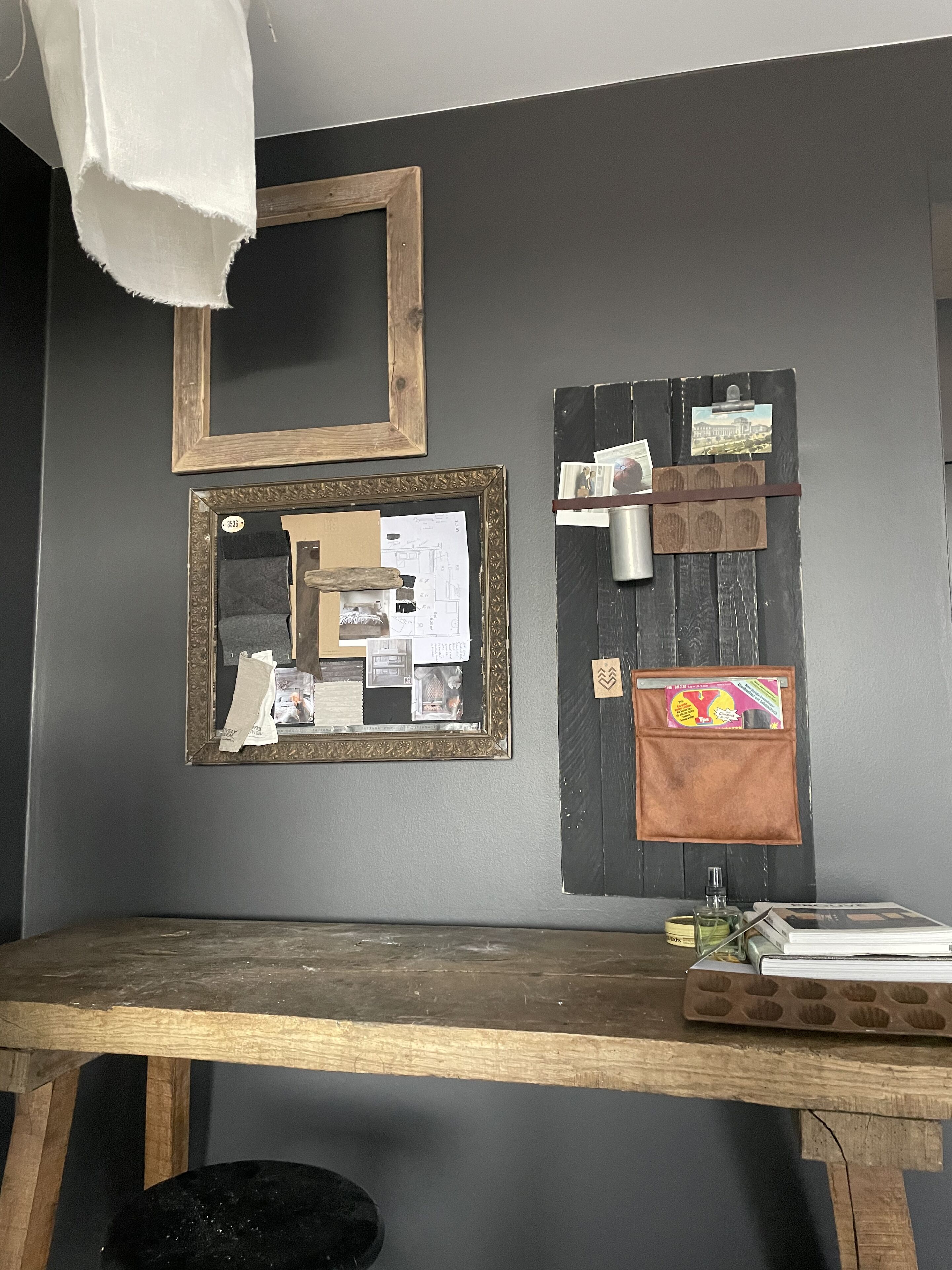 A room with a wooden desk, a mirror, and a bulletin board with papers and photos pinned to it.