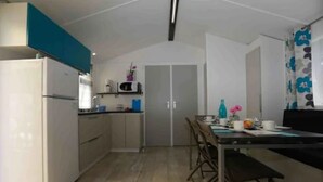 A compact kitchen with a refrigerator, microwave, and a dining area with a table and chairs. - Camping Milella (Olmeto)