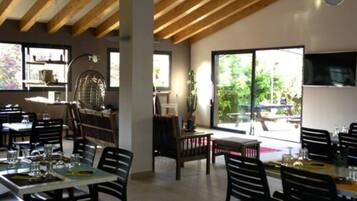 A restaurant with wooden ceiling beams, large windows, and black chairs. Tables are set with glasses and cutlery.