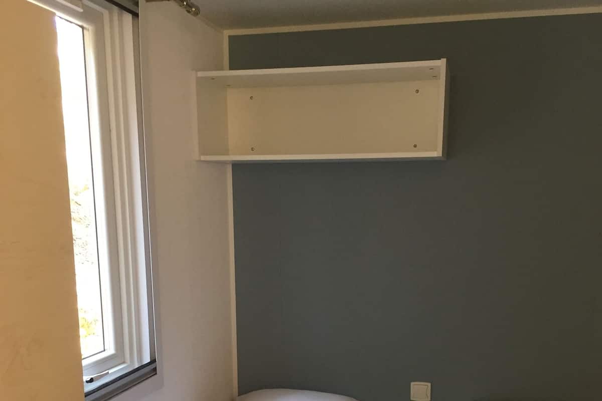 Habitación pequeña y funcional con dos literas y una cama individual, que cuenta con una ventana y un estante en la pared.