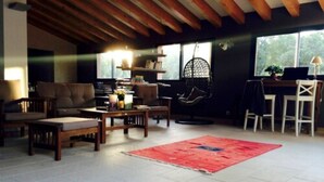 A cozy living room with a sofa, chairs, a coffee table, and a red rug. There is a hanging chair and a desk with a lamp. - Camping Milella (Olmeto)