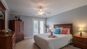 Een slaapkamer met een bed, een houten dressoir, een nachtkastje, een plafondventilator en een deur naar een balkon.