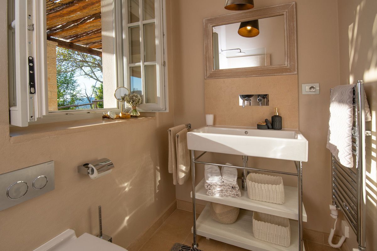Een badkamer met raam, wastafel, spiegel en handdoekrek.