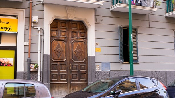 A building with a large wooden double door, a small window with shutters, and a sign with text. - B&B Sosta Flegrea (Naples)