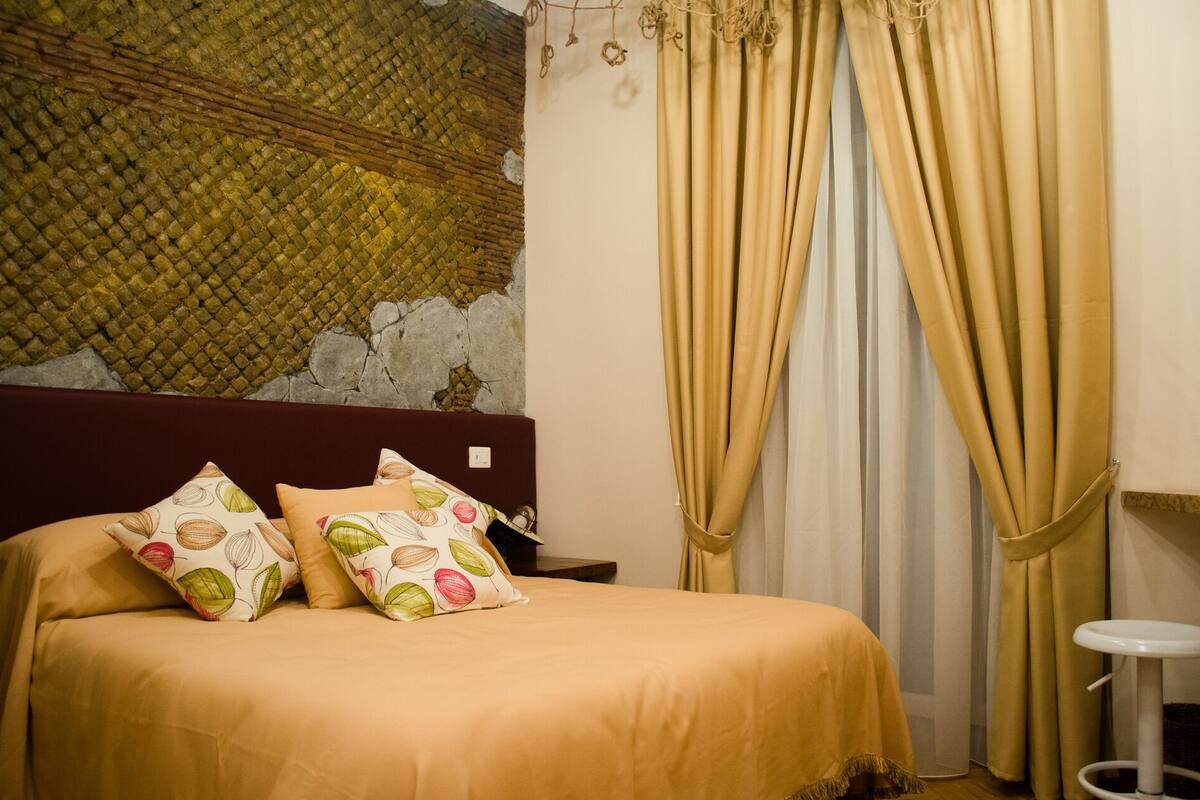Cama com almofadas estampadas, cabeceira e cortinas.