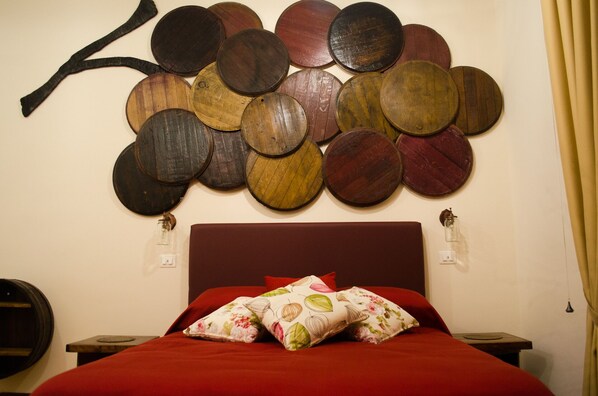 Una cama con colcha roja y almohadas florales, una pared con un mosaico circular de madera, y un cabecero de madera oscura.