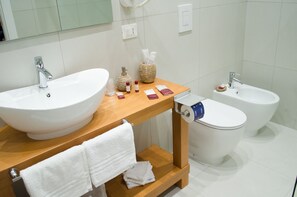 Un baño moderno con dos lavamanos, un bidé y un mueble de tocador de madera con artículos de aseo.