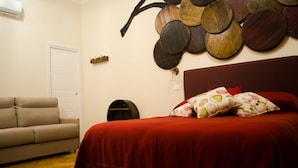 A bedroom with a red bedspread, a beige sofa, and a wall-mounted decorative piece. - B&B Sosta Flegrea (Naples)