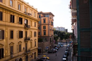 Vista de una calle en una ciudad con edificios de varios pisos, coches aparcados y un peatón.